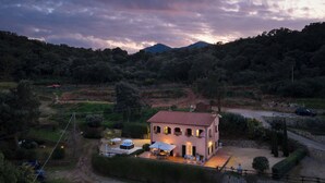 Una casa con tetto in tegole rosse, un patio con mobili da esterno e vista su un pendio boscoso.