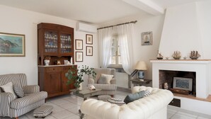 Un soggiorno con arredi a righe, un armadio in legno, un caminetto e un quadro raffigurante una scena costiera.