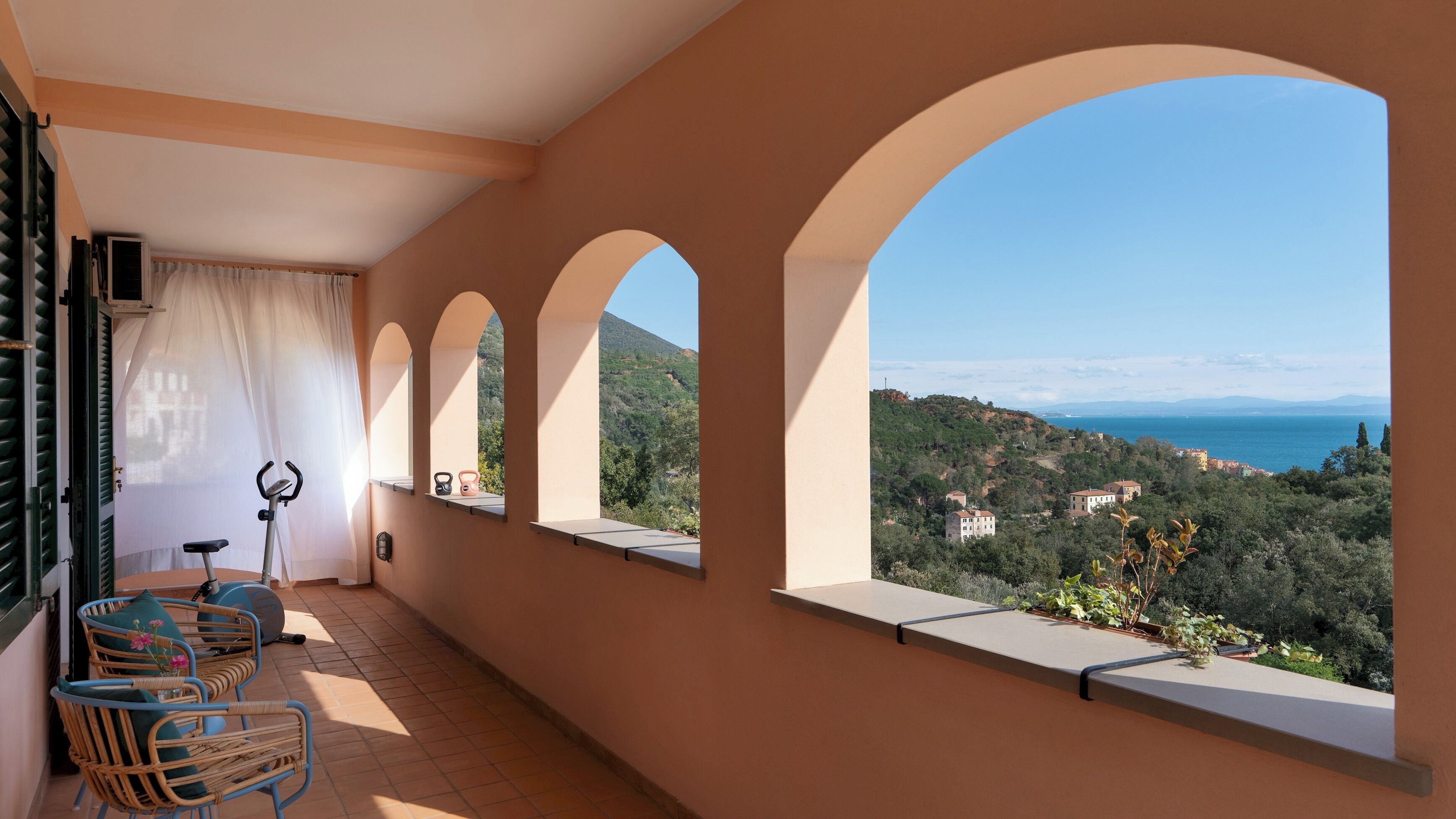 Un balcon donnant sur un paysage côtier, avec des meubles en osier et un tapis de course.