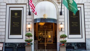 Entrada del Hotel Mayflower Park, con fachada clásica, dos banderas y un letrero de bienvenida.