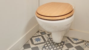 En toalett med ett trätoalettlock i ett badrum med mönstrade golvplattor.