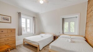 A bedroom with two single beds, a wooden dresser, a ceiling fan, and large windows. - Auberge du vieux pont (Saint-Raymond)