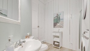 A bathroom with a sink, toilet, and a shelf with towels. - Auberge du vieux pont (Saint-Raymond)
