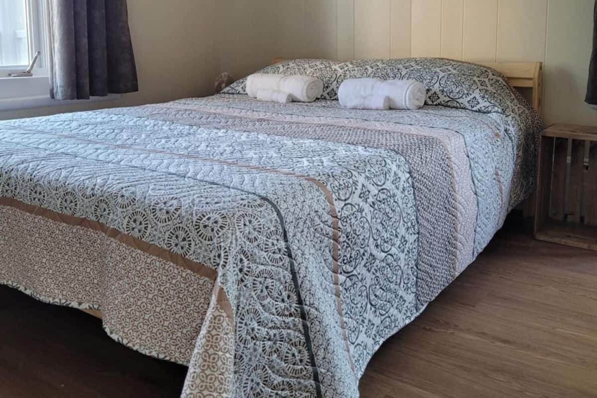 Un lit avec une couvre-lit à motifs, un tableau représentant une jetée accroché au mur et une fenêtre avec des rideaux.