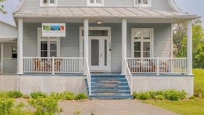 A two-story building with a porch, a front door, and a staircase leading to the entrance. - Auberge du vieux pont (Saint-Raymond)