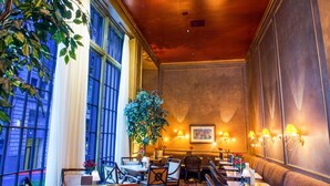 Un restaurant doté d’un haut plafond, de grandes fenêtres et d’une plante au centre. Les tables et les chaises sont disposées pour accueillir les clients.