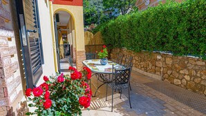 An outdoor patio with a table and chairs, a potted plant with red flowers, and a stone wall. - Apartment 'Casa Mariateresa' with Mountain View, Wi-Fi, and Air Conditioning (Vico Equense)
