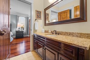 A bathroom with a granite countertop, wooden cabinetry, a large mirror, and a door leading to another room. - Family Retreat ~ Waterfront Luxury Home Sleeps 26 Comfortably (Centre)