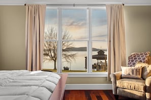 Une pièce dotée d’une grande fenêtre, d’un lit, d’une chaise et offrant une vue sur un quai et un lac.