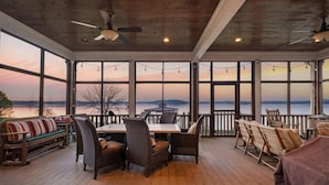 A covered outdoor area with a table and chairs, large windows, and a view of a body of water. - Family Retreat ~ Waterfront Luxury Home Sleeps 26 Comfortably (Centre)