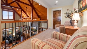 A spacious loft with a high ceiling, wooden beams, a view of the interior from the balcony, and a cozy seating area with striped cushions. - Family Retreat ~ Waterfront Luxury Home Sleeps 26 Comfortably (Centre)