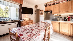 A kitchen with wooden cabinets, a dining table with a patterned tablecloth, and a television mounted above the counter.