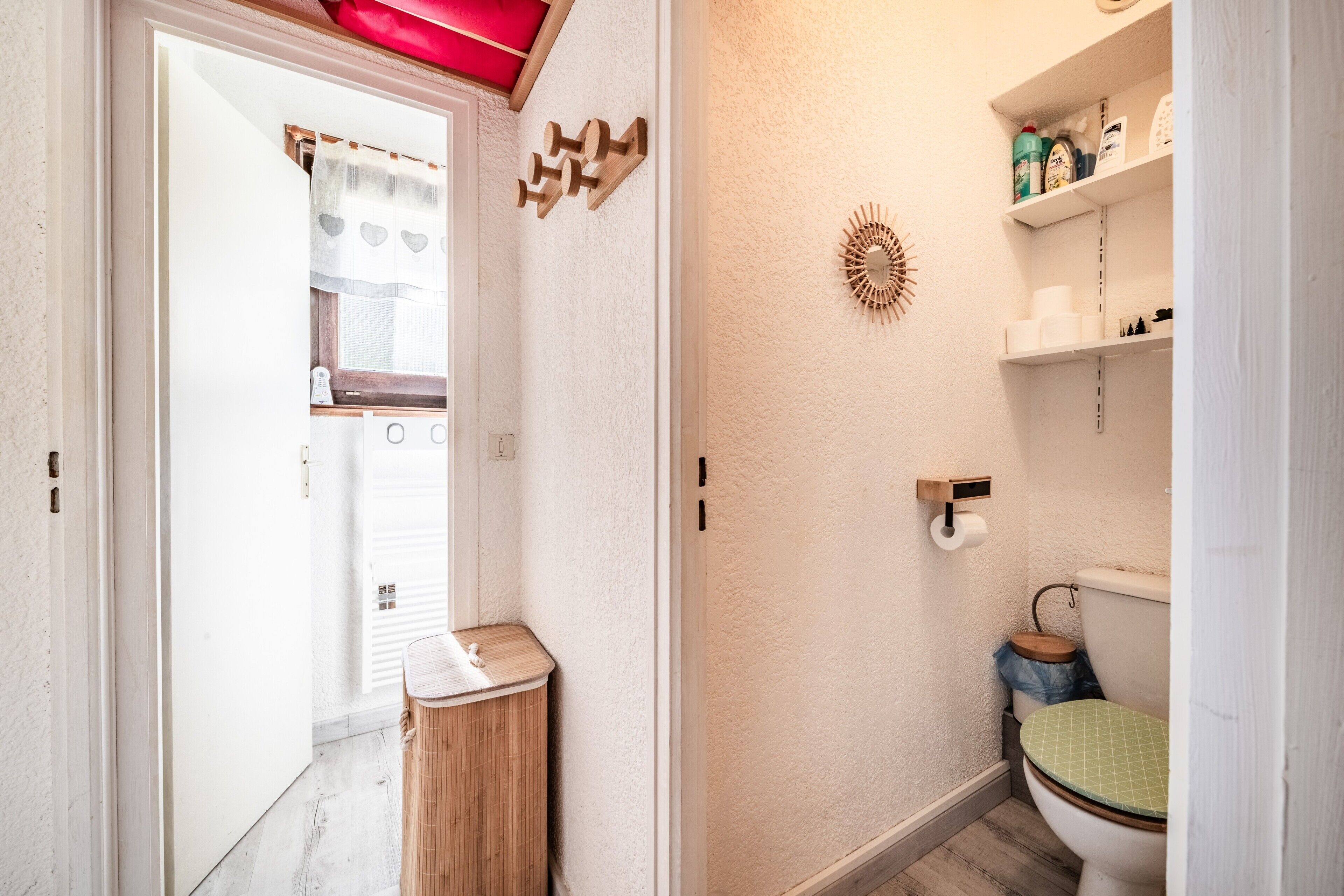 Een badkamer met toilet, een kleine prullenbak, een wandplank met toiletartikelen en een decoratief object aan de muur.