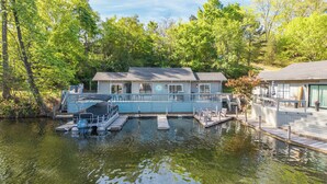 A lakeside cabin with a dock, a covered boat, and a deck area. - Lakefront Getaway w Boat Slip + Patio - Sleeps 8 - Fully Stocked - EV charger (Hot Springs)