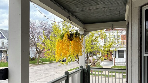 A covered porch with a hanging planter, a railing, and a view of the street. - Silver Swan in Riverwest! (Milwaukee)
