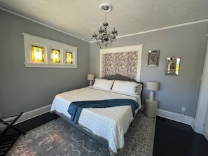 Une chambre à coucher avec un lit, un lustre, des lampes fixées au mur et un papier peint à motifs.