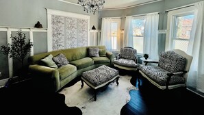 A living room with a green sofa, patterned armchairs, a white rug, and a chandelier. - Silver Swan in Riverwest! (Milwaukee)