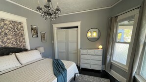 A bedroom with a bed, dresser, chandelier, and a window with curtains. - Silver Swan in Riverwest! (Milwaukee)