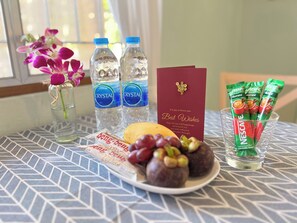 A table with bottled water, a card, a plate with snacks, and a glass with Nescafe packets. - Cozy Local-Style Home in a Quiet Area, 8 Minutes from the Beach (Surat Thani)