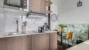 A compact kitchen with a microwave, sink, and wooden cabinets. - Charming Studio Apartment 2P - Nation (Paris)