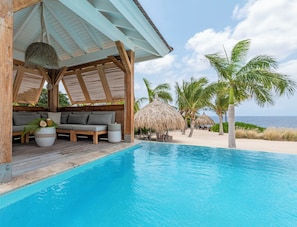 A poolside area with a wooden deck, a sofa, and a thatched umbrella.