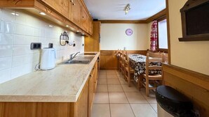Una cocina con armarios de madera, encimera de mármol, cafetera y comedor con mesa y sillas.