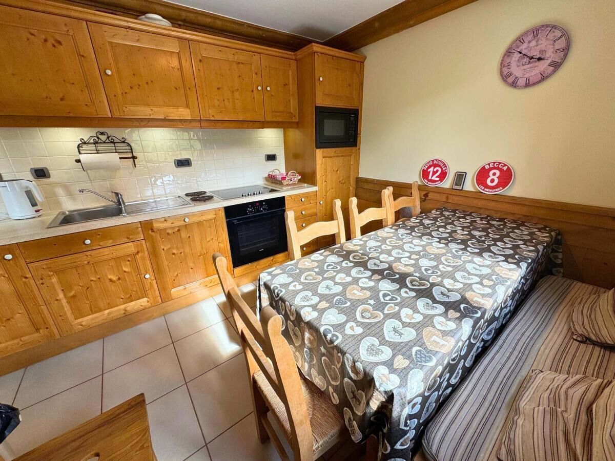 Una cocina compacta con armarios de madera, un microondas y una zona de comedor con mantel estampado.