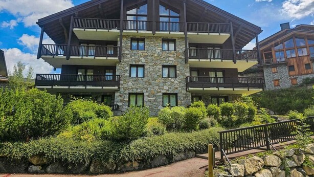 Un edificio de varios pisos con balcones, fachada de piedra y un camino que lleva a la entrada.