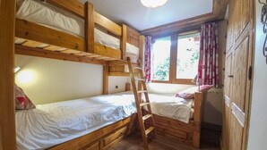 Habitación con literas de madera, una escalera, una ventana con cortinas y un armario.