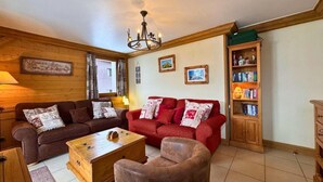 Una sala de estar acogedora con un sofá marrón, un sofá rojo, una mesa de centro de madera y una estantería de madera.