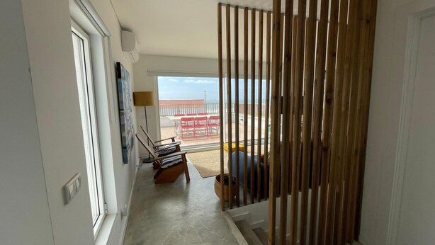 Habitación con puerta corredera que da a un balcón con sillas rojas y una mesa, televisor de pantalla plana montado en la pared y aire acondicionado instalado en el techo.