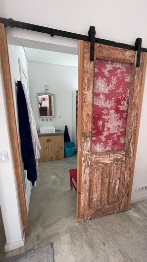 A room with a sliding barn door, a sink, a mirror, and a red chair. - Praia das Maças - Azenhas do Mar V4 Beachfront Home (Colares)