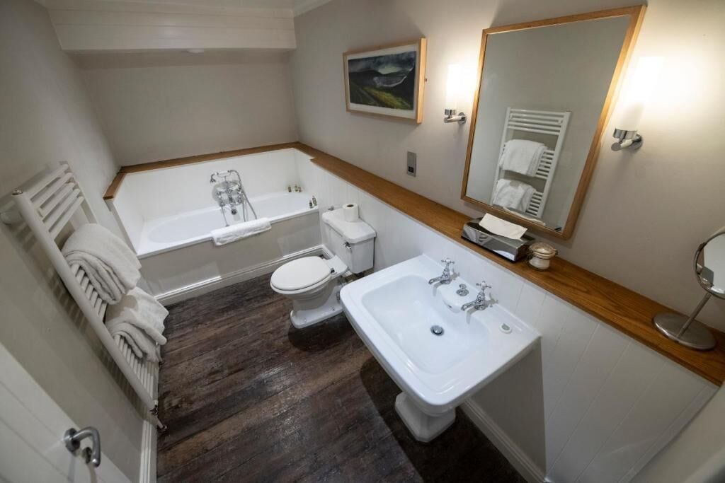 A bathroom with a bathtub, toilet, and sink, wooden floor, and a mirror.
