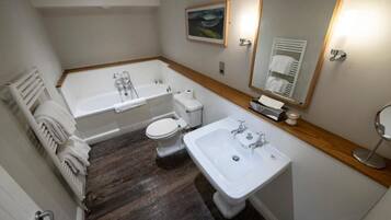 A bathroom with a bathtub, toilet, and sink, wooden floor, and a mirror.