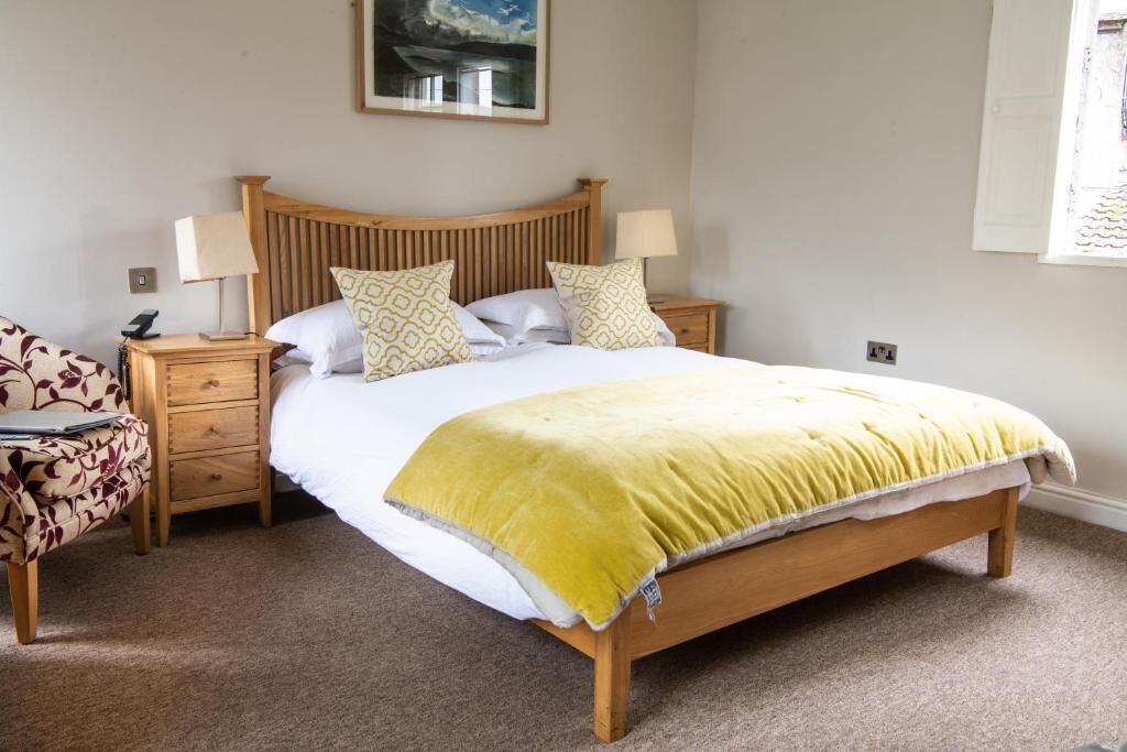 A bedroom with a wooden bed, two bedside tables, a nightstand, a patterned armchair, and a painting on the wall.