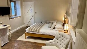 A bedroom with a bed, a chair, a desk, a television, and a door. - Wheelwrights Arms (Monkton Combe)