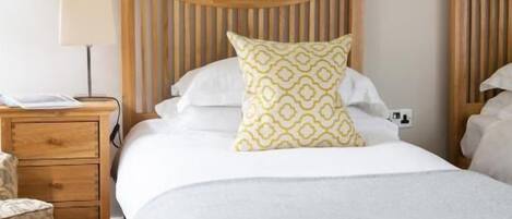 Un dormitorio con cabecera de madera, cama con manta gris y almohada amarilla, mesita de noche con lámpara y un cuadro colgado en la pared.