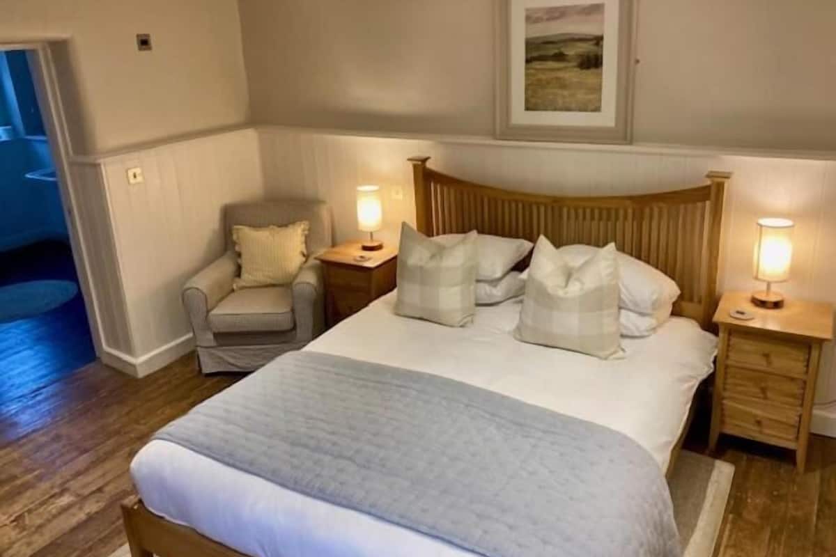 Una camera da letto con un letto, due comodini con lampade, una sedia e un quadro appeso alla parete.