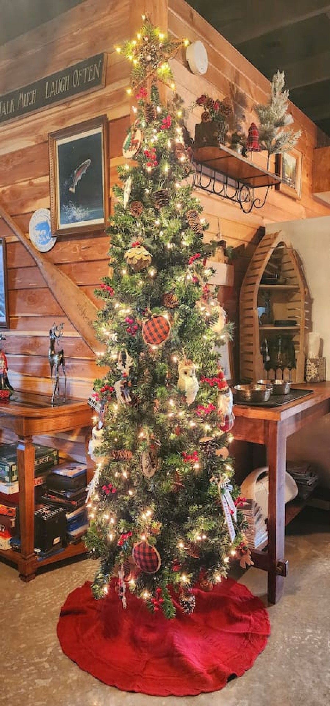 A decorated Christmas tree in a room with wooden walls, a fireplace, and a shelf with various items.