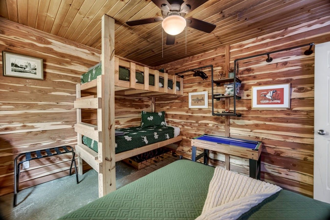 A bunk bed room with a desk and shelves, wooden walls, and ceiling fan.