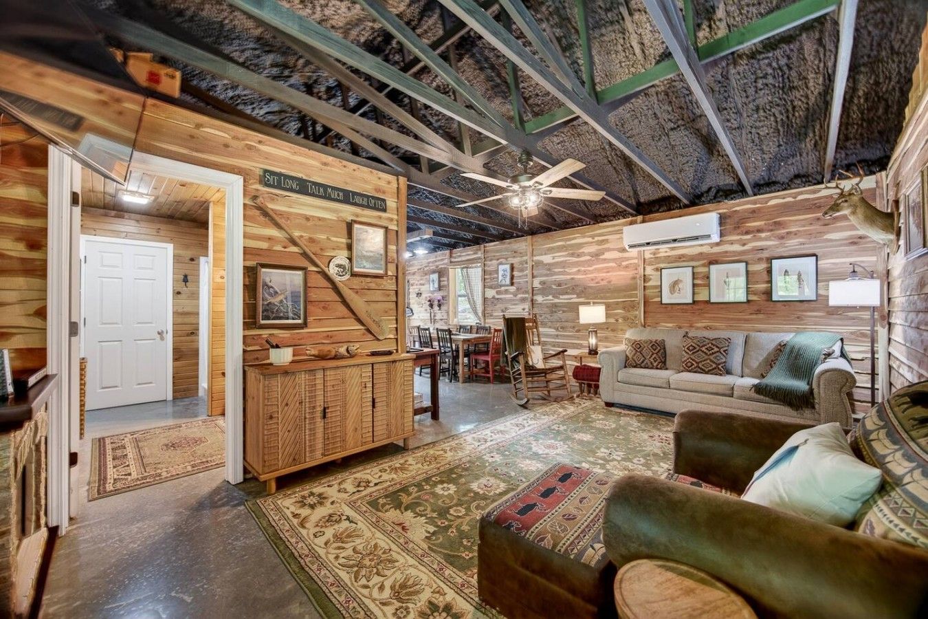 A rustic interior with wooden walls, a dining area, and a seating area with a sofa and ottoman.