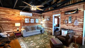 Interior acollidor d'una cabana de fusta amb un sofà, una butaca i un llit.