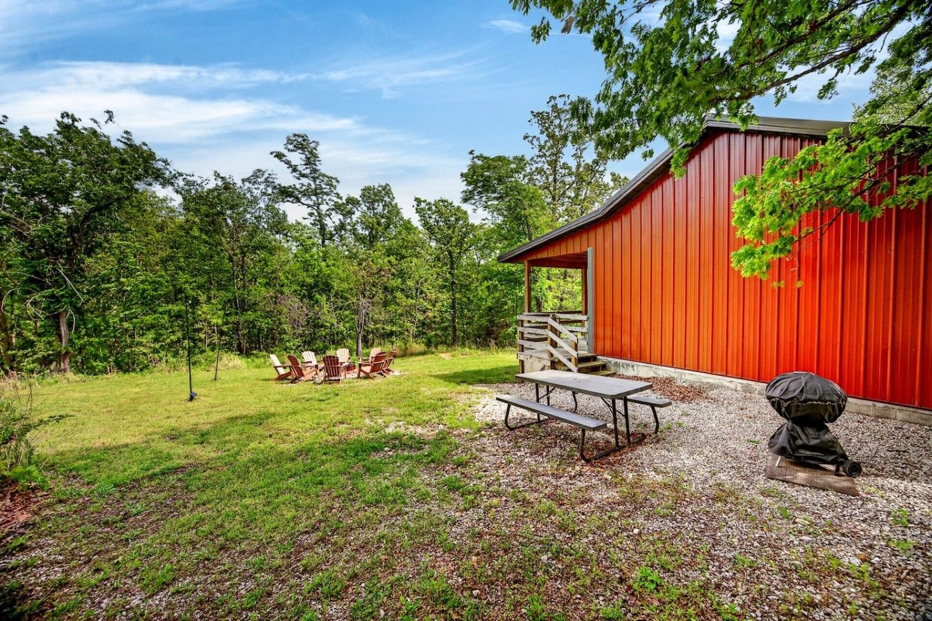 A red building with a picnic table and chairs in a grassy area.
