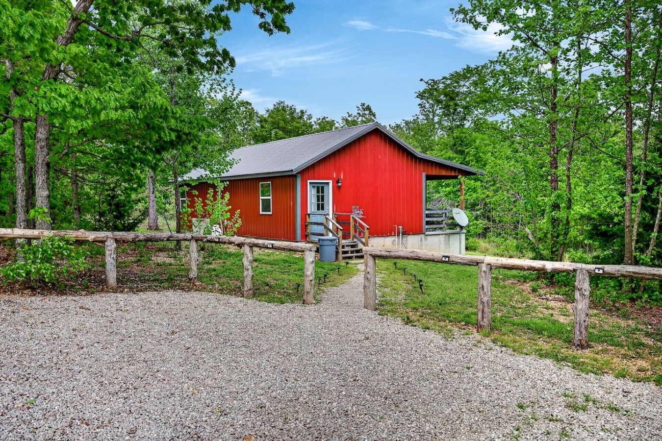 A red building with a gravel path leading to it, surrounded by trees.