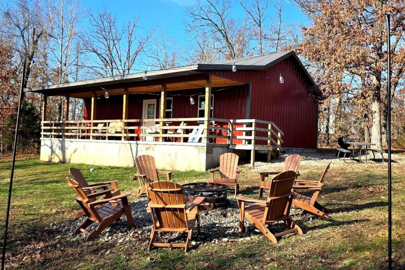 A red cabin with a porch, surrounded by Adirondack chairs and a fire pit.