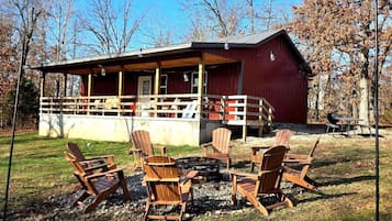A red cabin with a porch, surrounded by Adirondack chairs and a fire pit.
