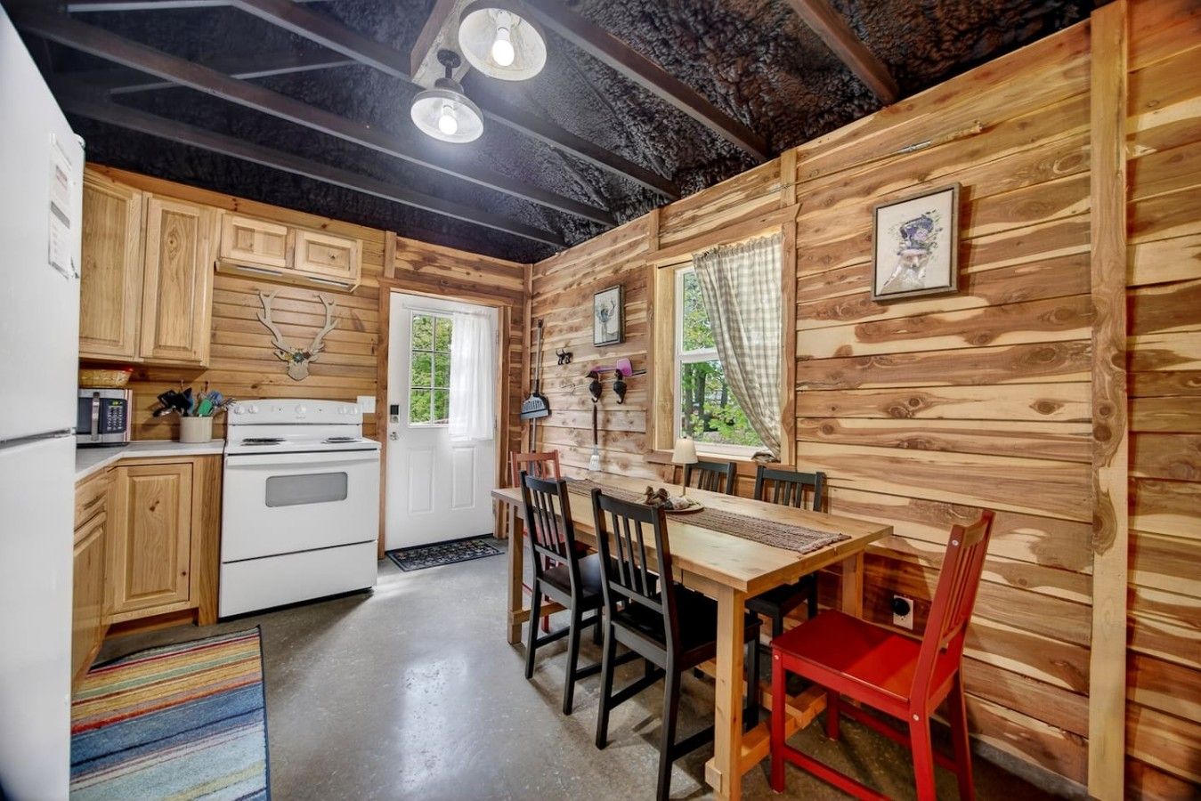 A cabin-style kitchen with wooden walls, a dining area with a table and chairs, and a white stove.