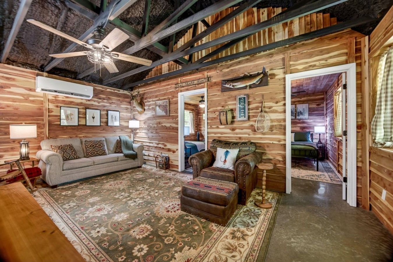 A rustic cabin interior with a ceiling fan, a sofa, a leather armchair, and a bed.