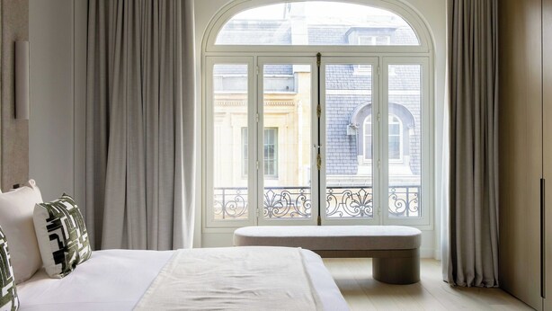 A hotel room with a large arched window, a bed, a bench, and a view of buildings outside. - Luxury Flat -2br/6p- Madeleine/saint Honore (Paris)