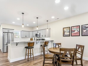 A modern kitchen with white cabinets, stainless steel appliances, and pendant lighting. There are three framed posters on the wall.